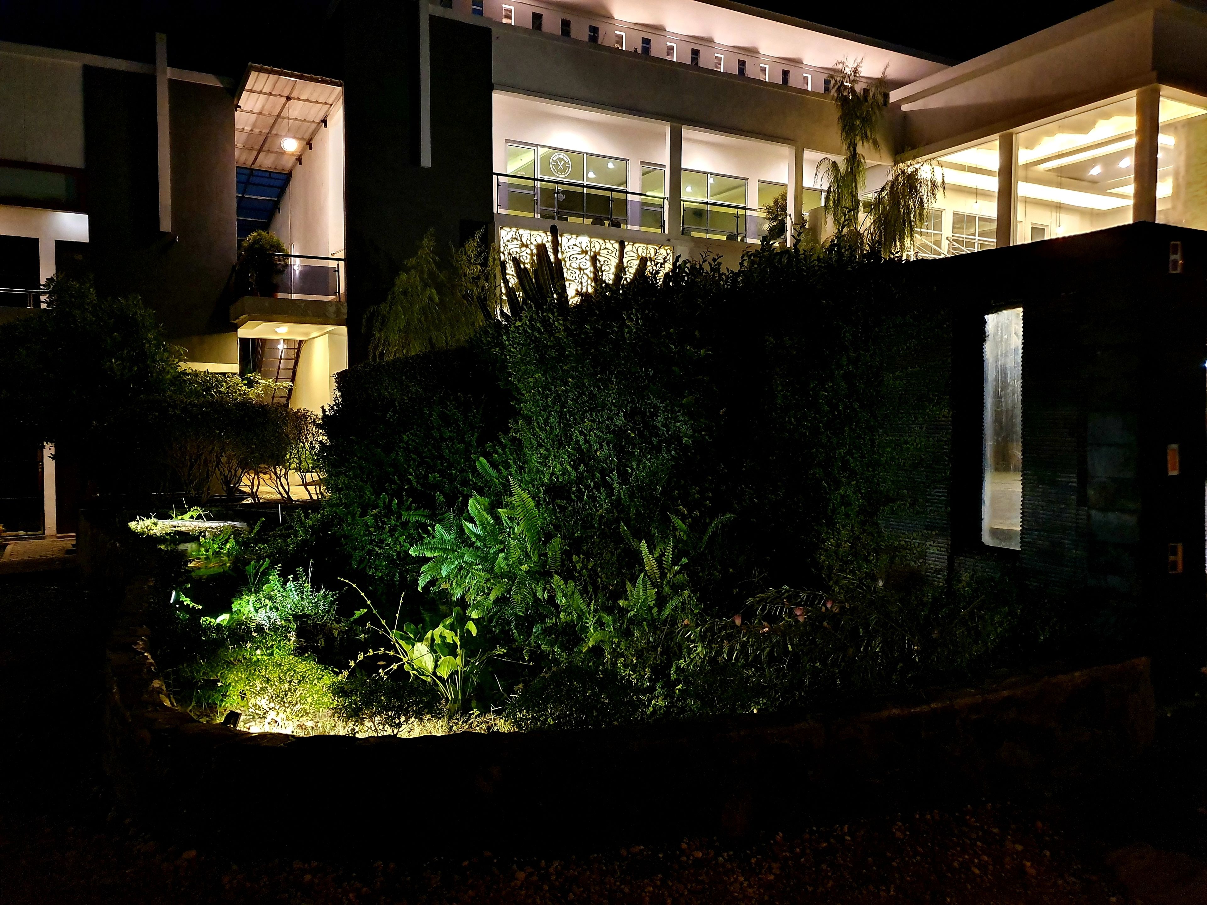 A modern building with a well-lit entrance, a covered outdoor area with plants, and a staircase leading to an upper level.