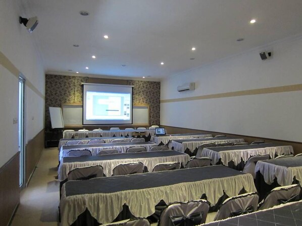 A conference room with rows of tables and chairs, a projector screen, and a whiteboard.