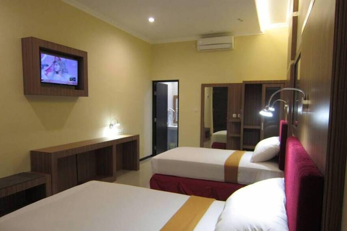 A hotel room with two beds, a TV mounted on the wall, a desk, and a wardrobe.