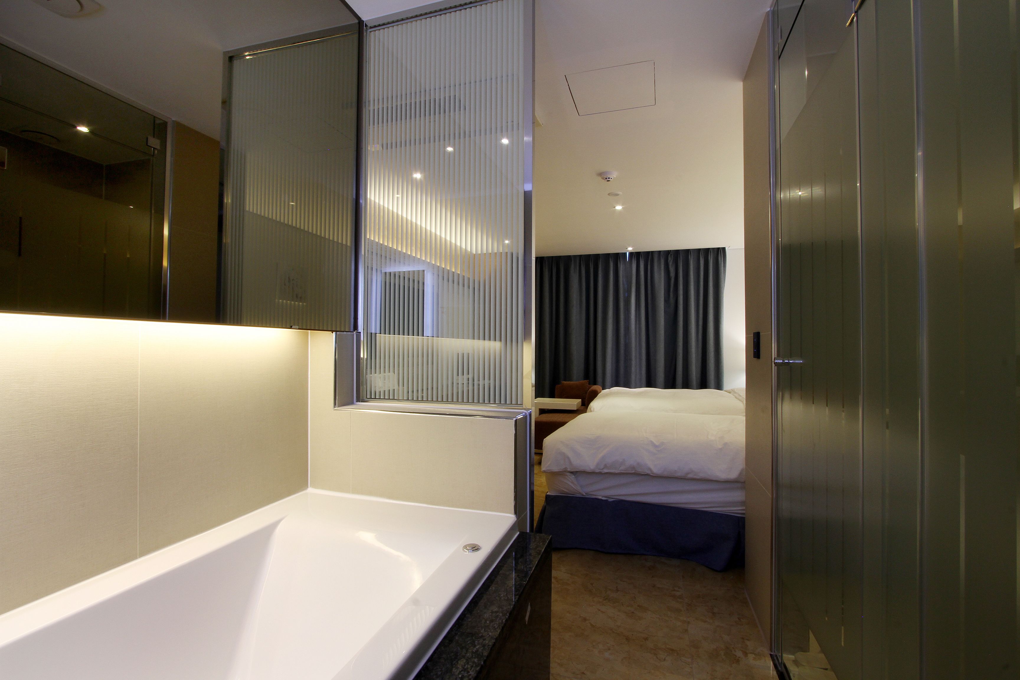 Habitación de hotel con un espejo grande, una bañera, una cama con dos almohadas y un armario.