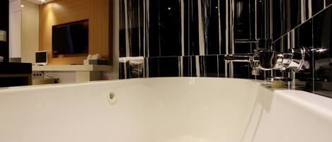 A modern bathroom with a large bathtub, a wooden vanity, and a large mirror.