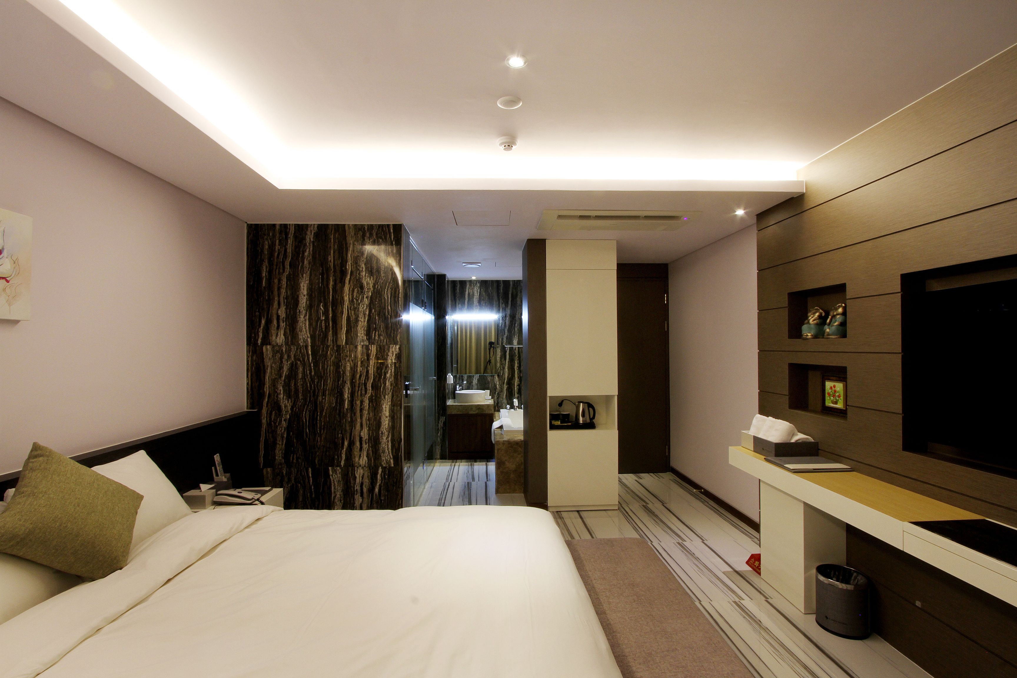 Une chambre d’hôtel moderne dotée d’un grand lit, d’une coiffeuse avec un miroir, d’une télévision et d’un petit bureau avec une lampe.
