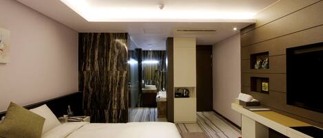 Une chambre d’hôtel moderne dotée d’un grand lit, d’une coiffeuse avec un miroir, d’une télévision et d’un petit bureau avec une lampe.