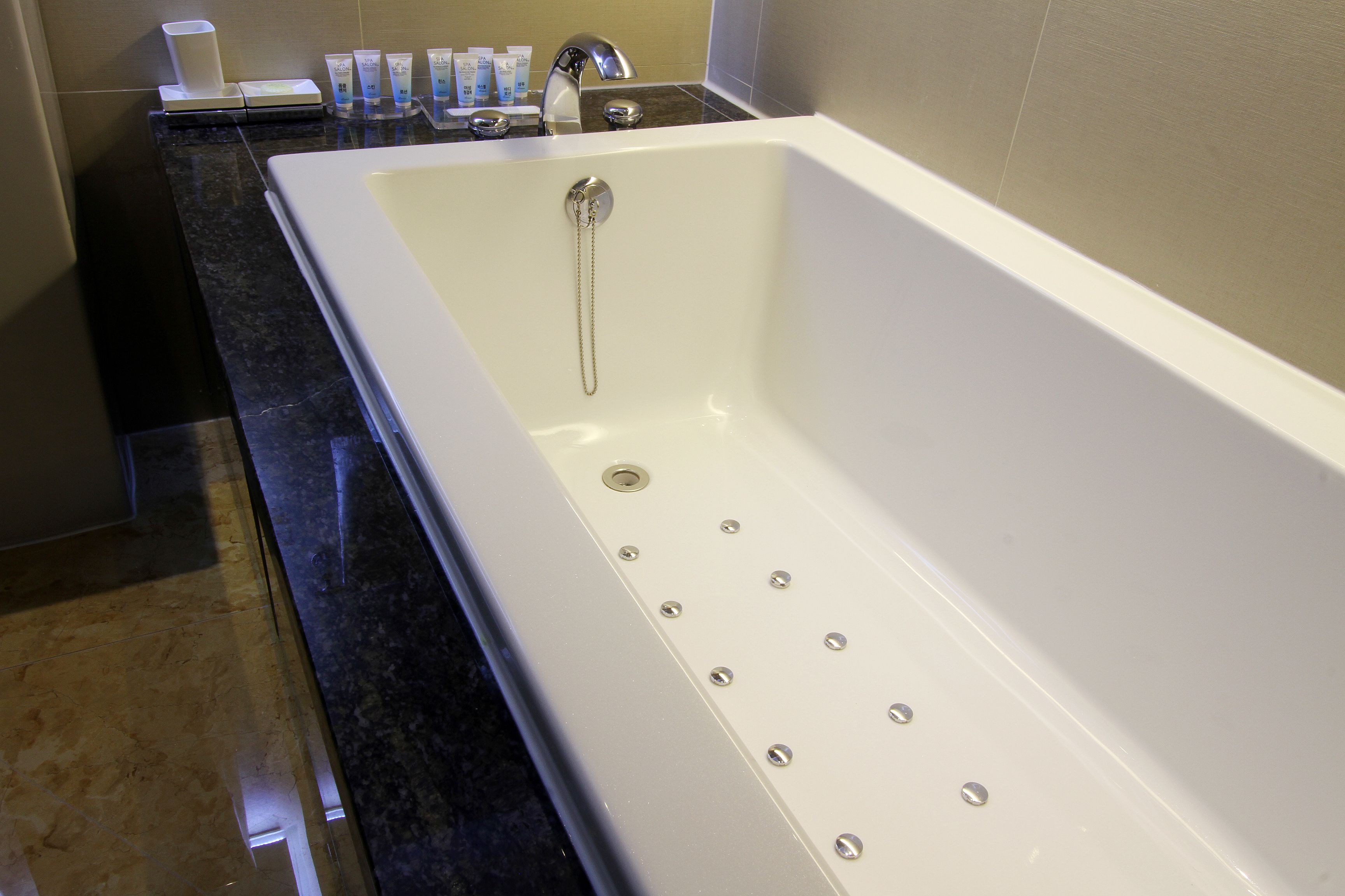 Un baño moderno con una bañera blanca grande, una encimera de mármol negro y un juego de artículos de aseo en la encimera.