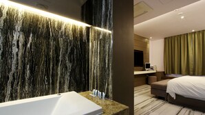 A modern bathroom with a marble wall, a large bathtub, and a vanity with toiletries.