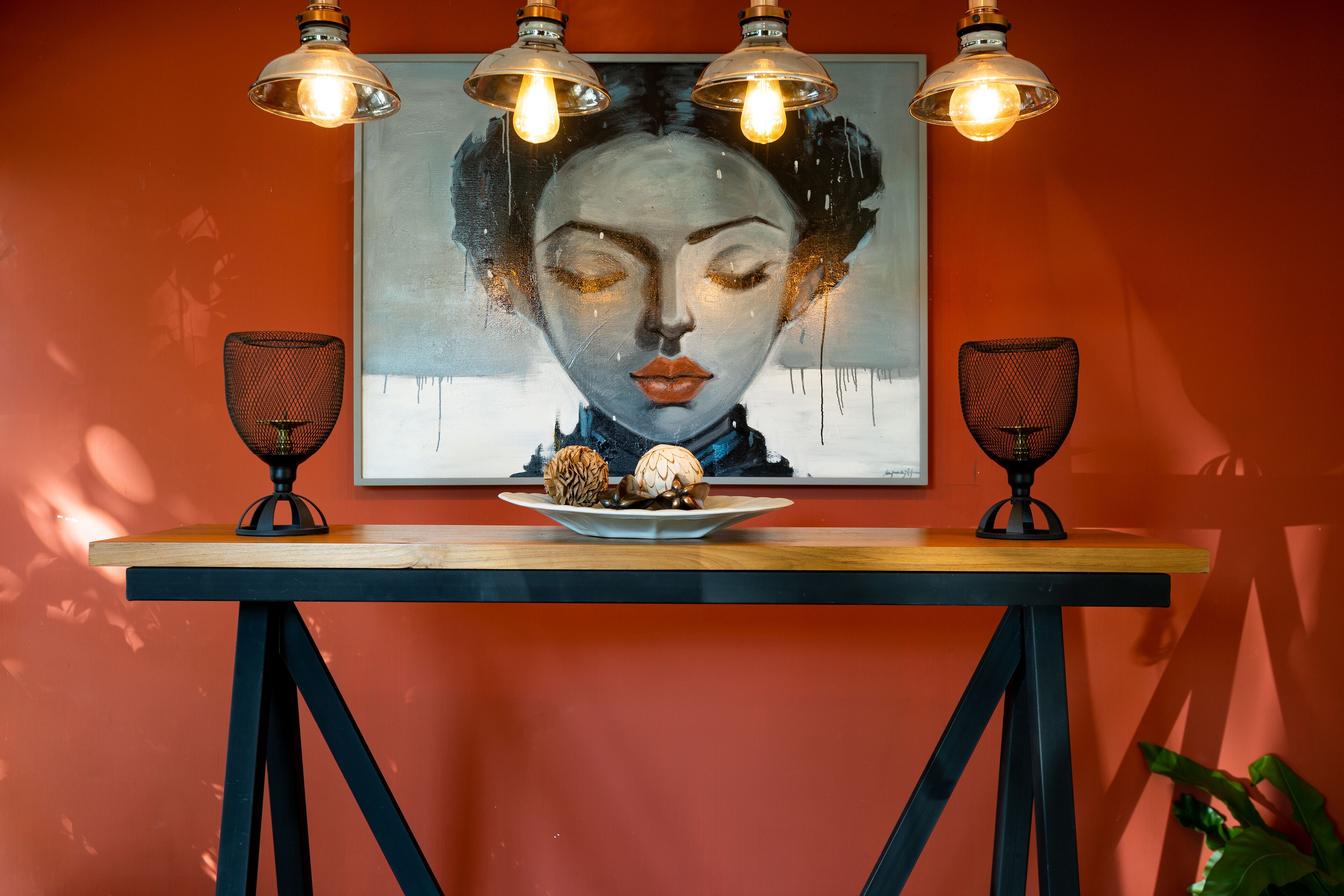 A table with a plate of food, two black mesh lamps, and a painting on the wall.