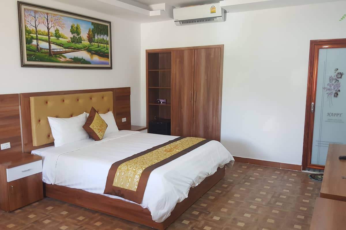 A neatly arranged bedroom with a bed, wooden headboard, bedside tables, a wardrobe, and a painting on the wall.