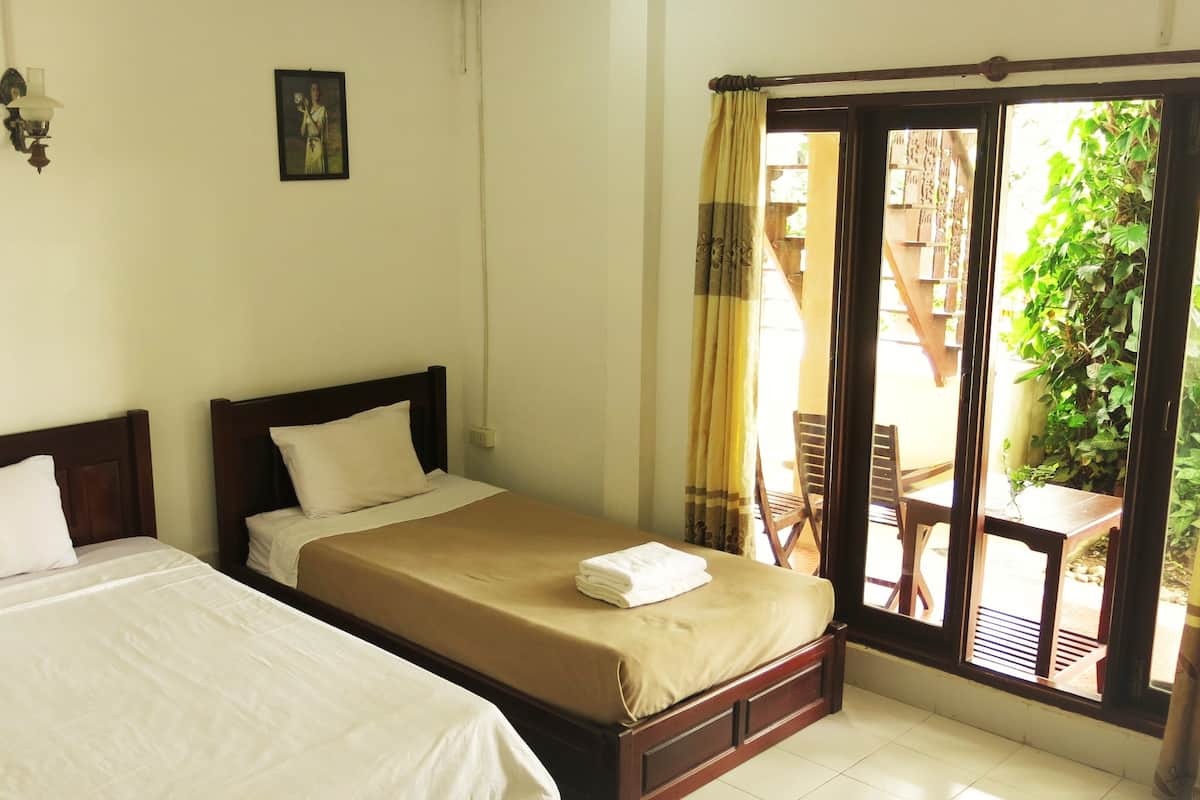 A room with two beds, a window with curtains, and a view of the outside.
