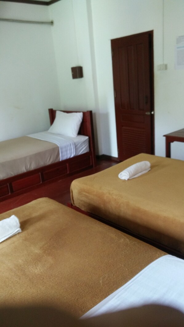 A room with two single beds, one with a wooden headboard and the other with a plain headboard. There is a wooden door and a small table in the room. - Vang Vieng Sunrise View Resort (Vang Vieng)