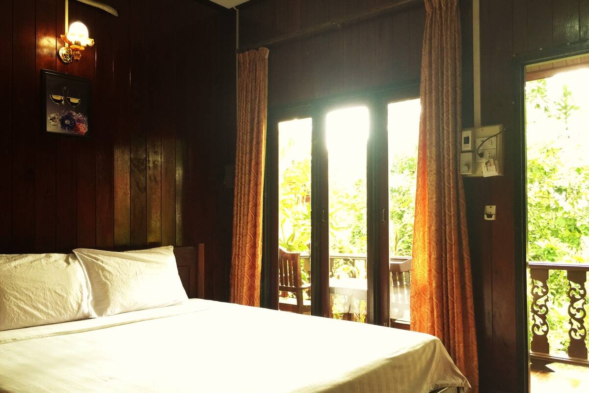 A bedroom with a bed, a nightstand, a wall-mounted lamp, and a window with curtains.