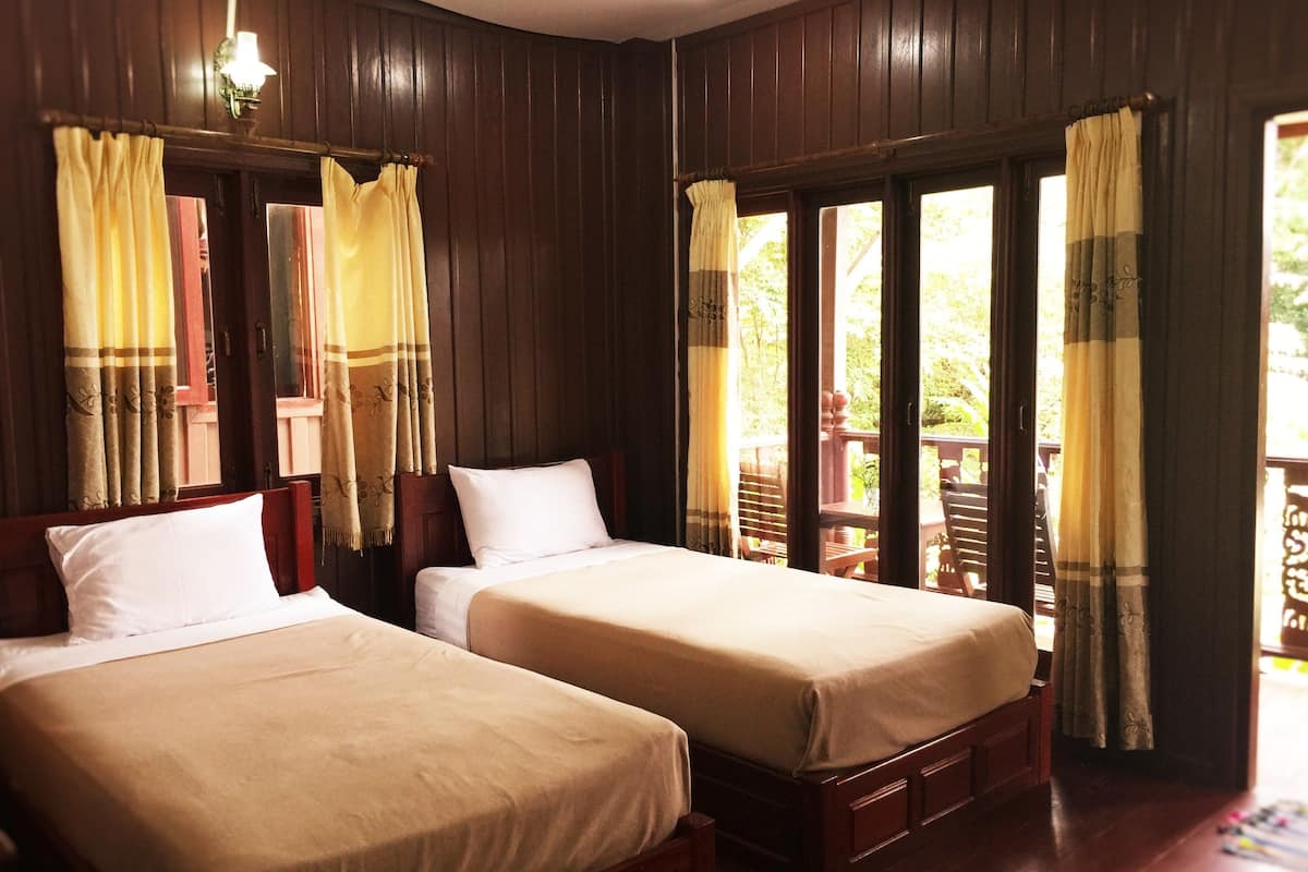 Two single beds with wooden headboards and white bedding in a room with dark wooden walls and large windows with curtains.