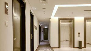 Un pasillo de hotel con puertas, una alfombra estampada y un piso de baldosas limpias.