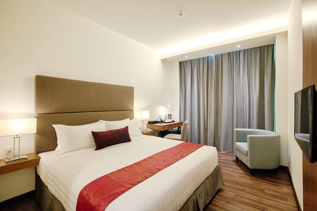 A hotel room with a large bed, a desk, a chair, and a TV.