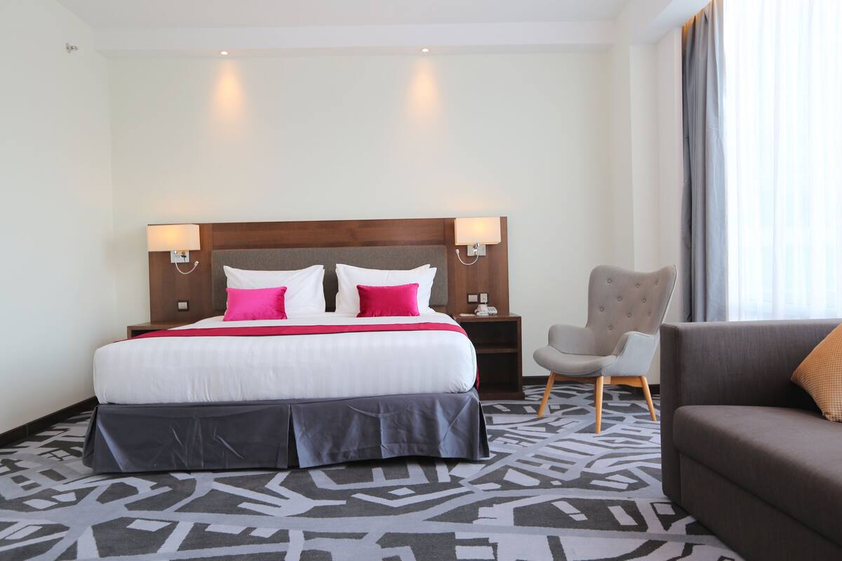 A hotel room with a large bed, two bedside lamps, a chair, and a sofa.
