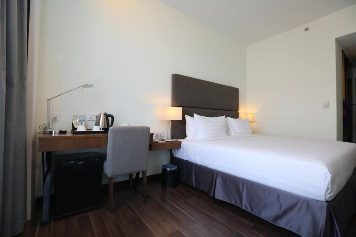 A hotel room with a bed, a desk, a chair, a lamp, and a coffee machine.