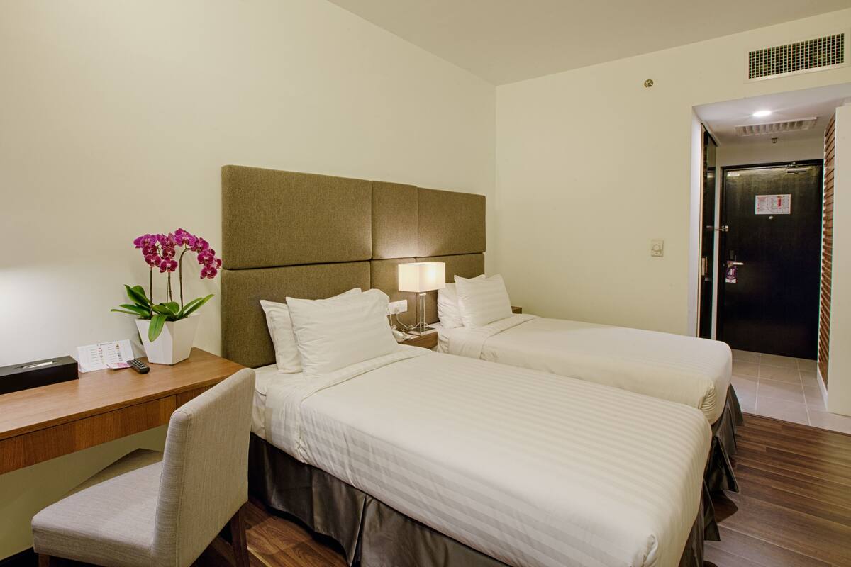 A hotel room with two beds, a desk, a chair, a lamp, and a potted orchid.