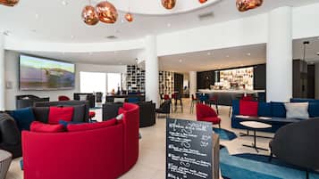 Un moderno hall de hotel con asientos rojo y negro, una zona de bar y una pantalla grande que muestra una vista panorámica.
