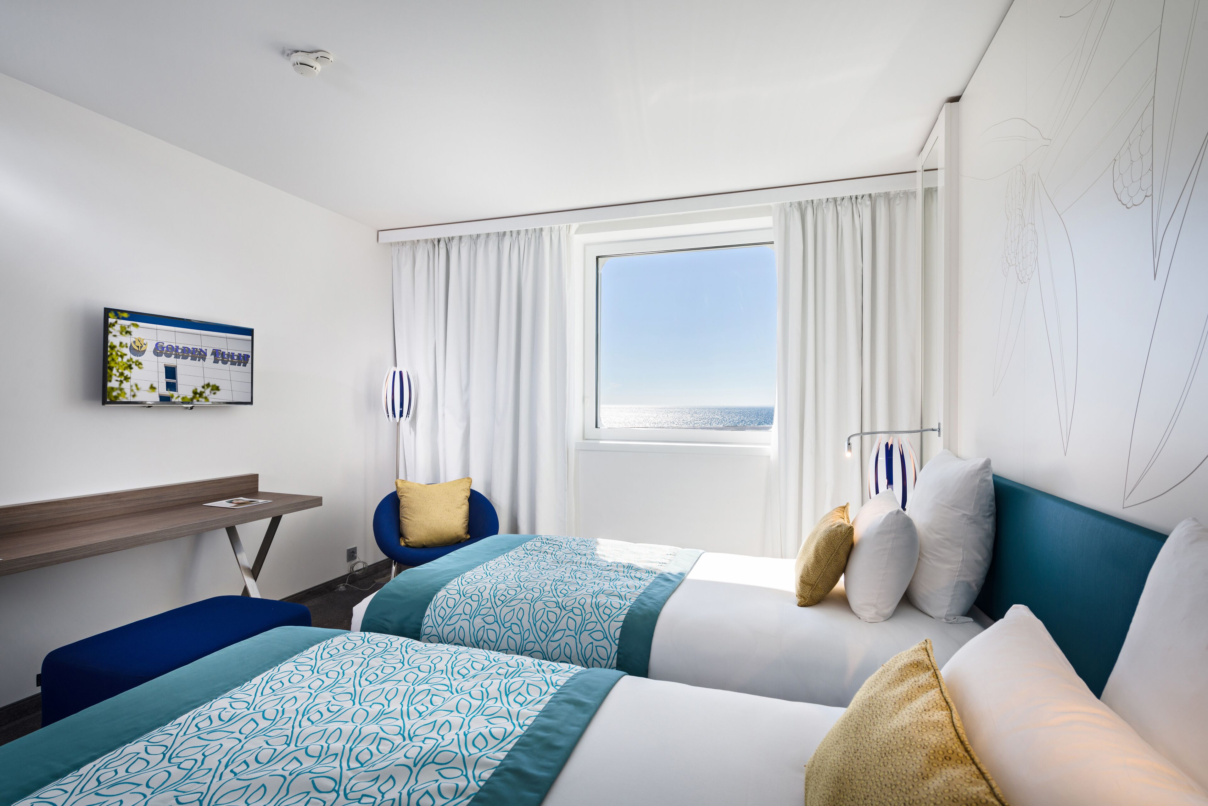 Une chambre d’hôtel avec deux lits, une télévision, un bureau et une fenêtre avec des rideaux.
