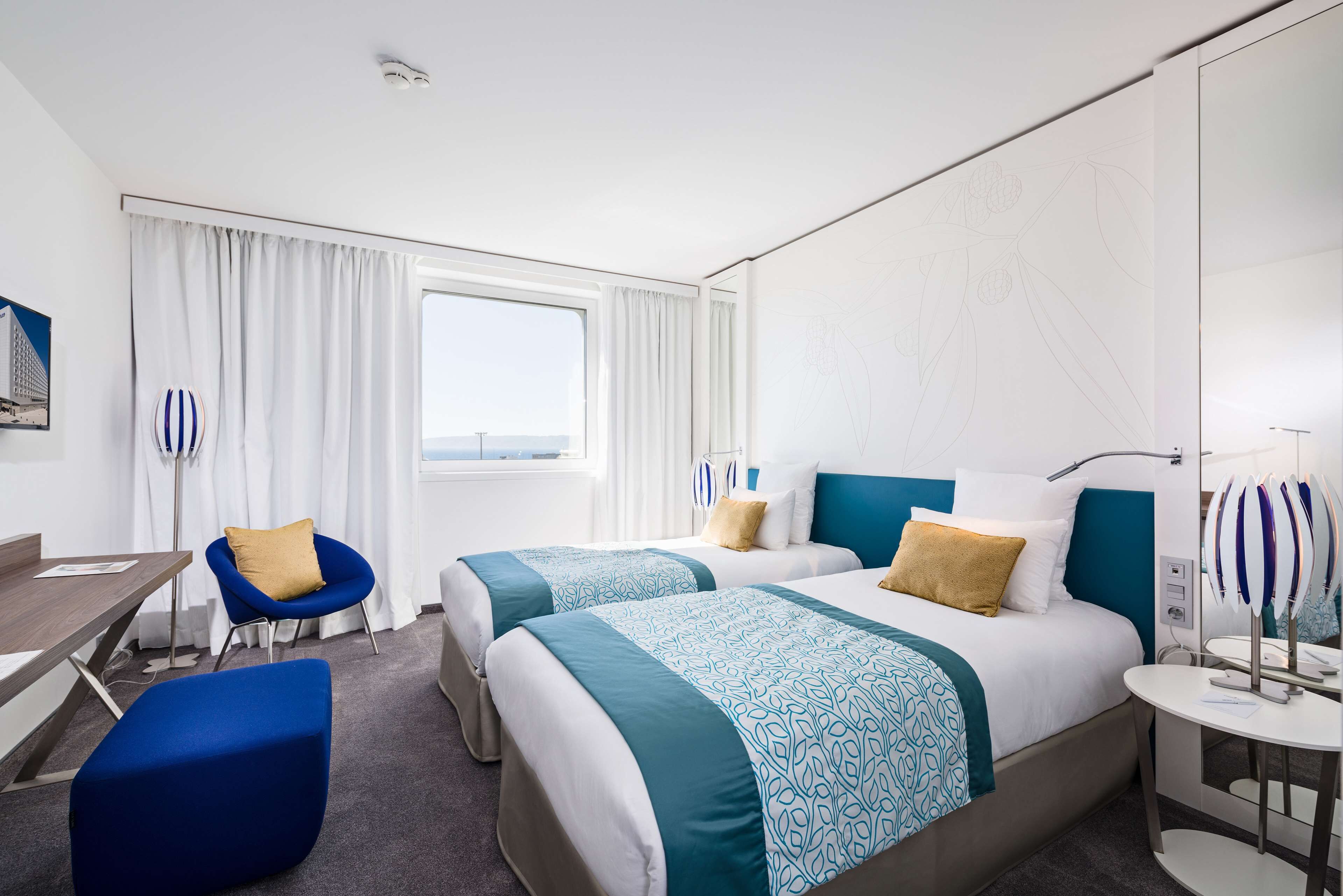 A hotel room with two beds, a desk, a chair, and a window with curtains.