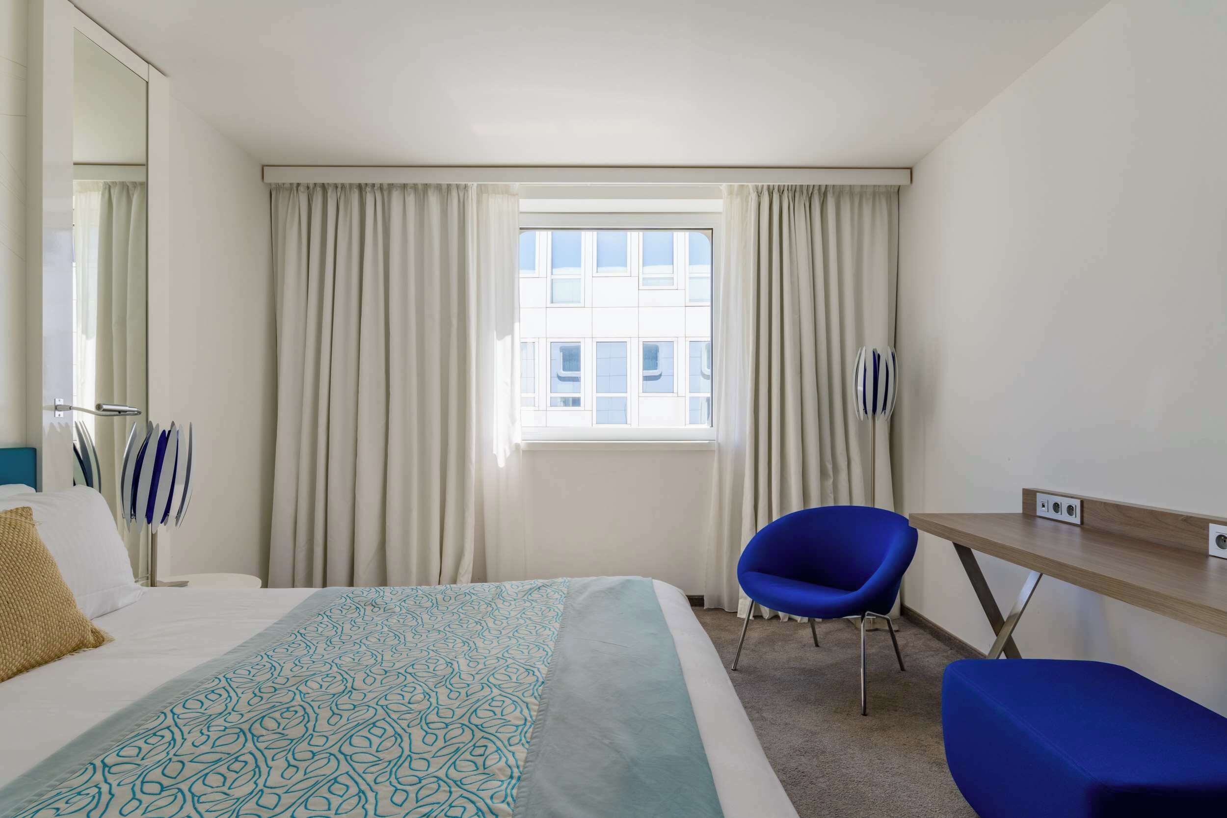 Habitación de hotel con cama, escritorio, silla y ventana con cortinas.