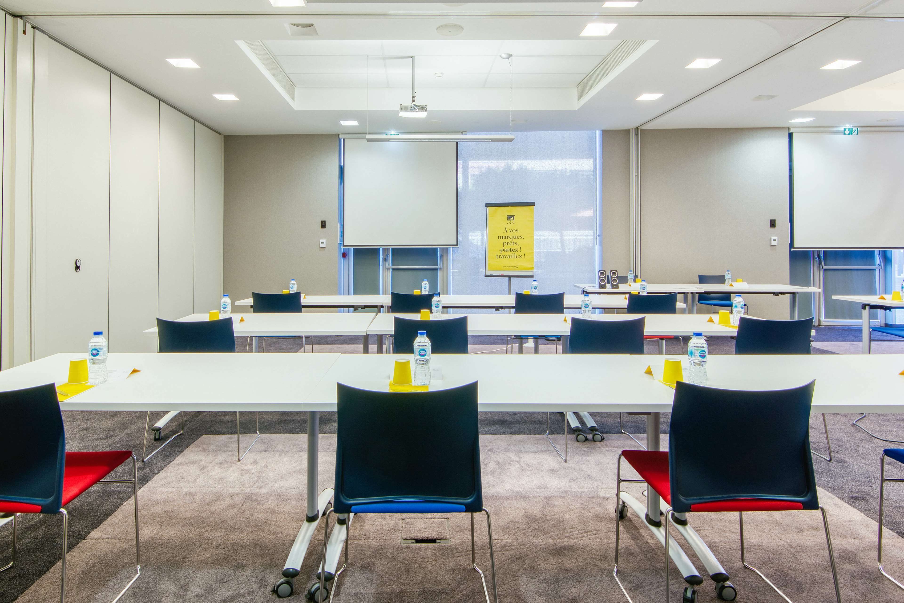 Ein Konferenzraum mit einem langen Tisch, Stühlen und einer Projektionsleinwand.
