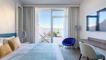 Habitación de hotel con cama, escritorio, silla, televisión y balcón con vistas.