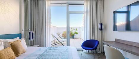 A hotel room with a bed, a desk, a chair, a TV, and a balcony with a view.