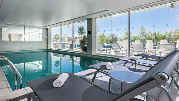 Área da piscina com espreguiçadeiras, piscina envidraçada e vista para o exterior.