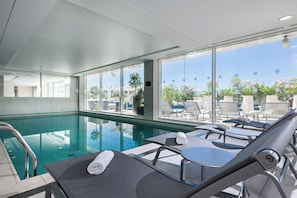 Un espace piscine doté de chaises longues, d’une piscine à moitié fermée par des parois en verre et offrant une vue sur l’extérieur.
