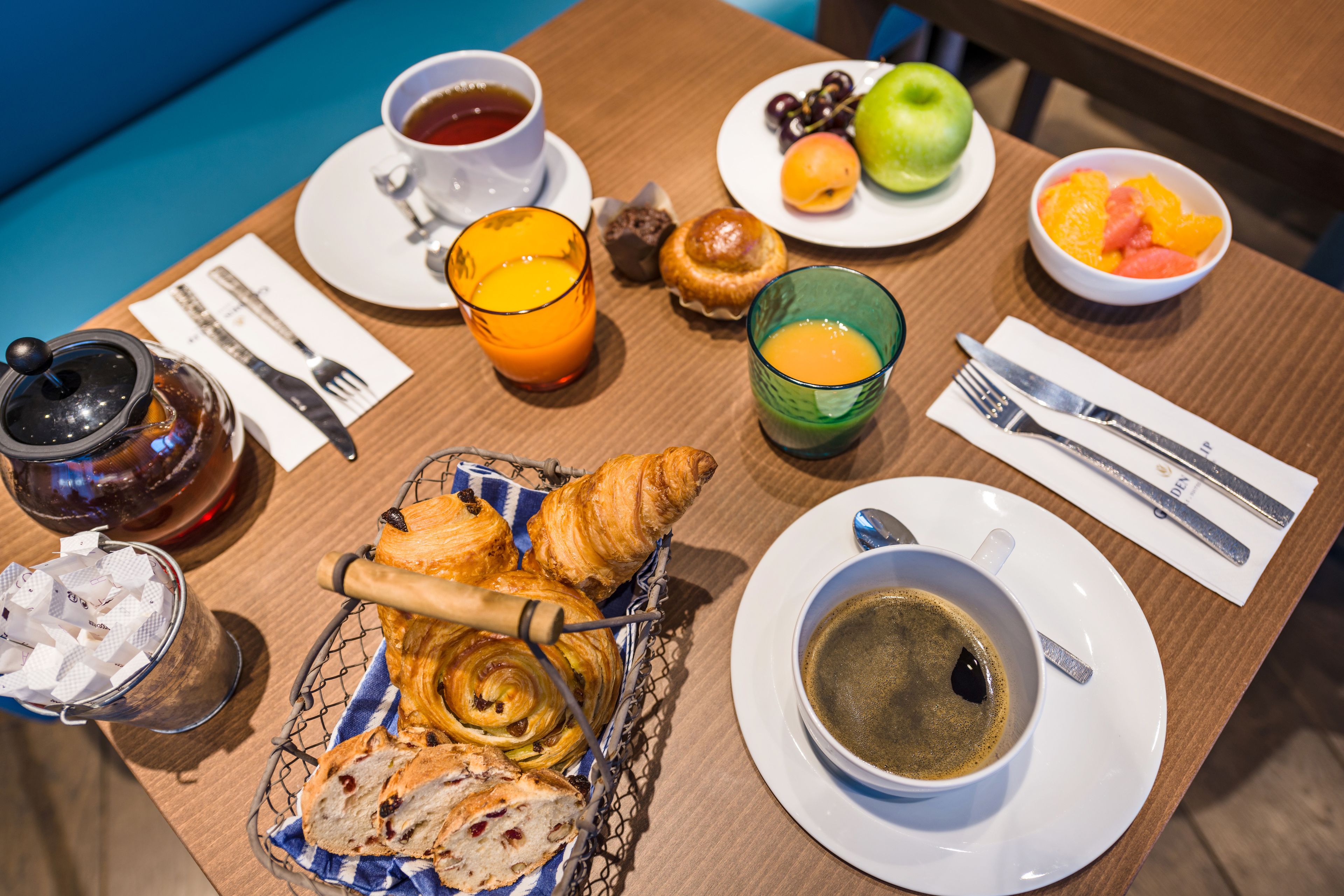 Eixam de matí amb croissants, pastissos, fruita, cafè i te sobre una taula de fusta.
