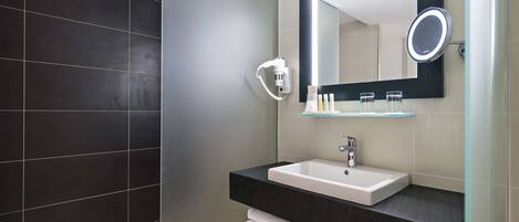 Een moderne badkamer met een donkere betegelde muur, een wit wastafelmeubel met spiegel en een plank met handdoeken.