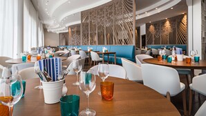 Restaurante moderno com mesas redondas, cadeiras e uma parede decorativa.
