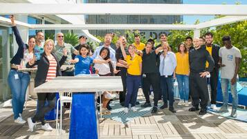 A group of people posing in an outdoor area with a wooden deck, a table, and a blue chair.