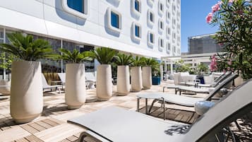 Zona relax su un tetto con poltrone e piante in vaso, con vista su un edificio moderno e una facciata geometrica.