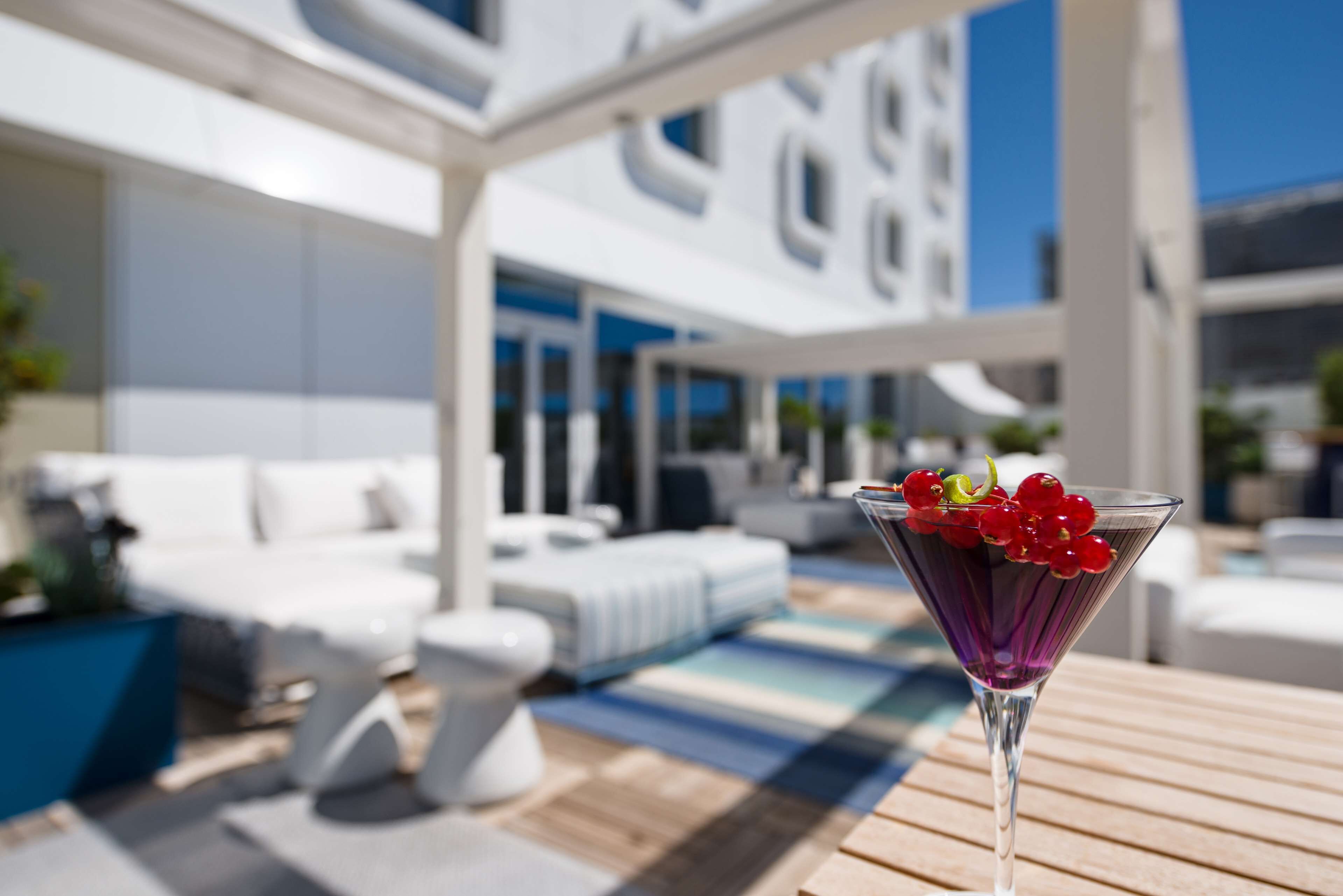 Un área de estar moderna al aire libre con piscina, muebles blancos y cielo despejado.
