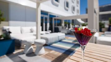 Un área de estar moderna al aire libre con piscina, muebles blancos y cielo despejado.