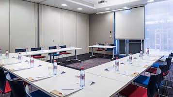 Ett konferensrum med långa bord, stolar, vattenflaskor och en projektorduk.