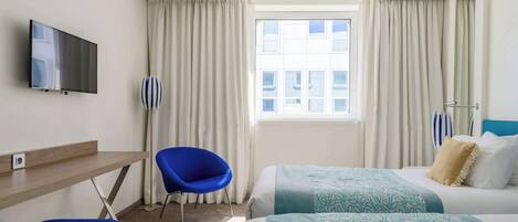 A hotel room with a bed, a desk, a chair, a TV, and a window with curtains.