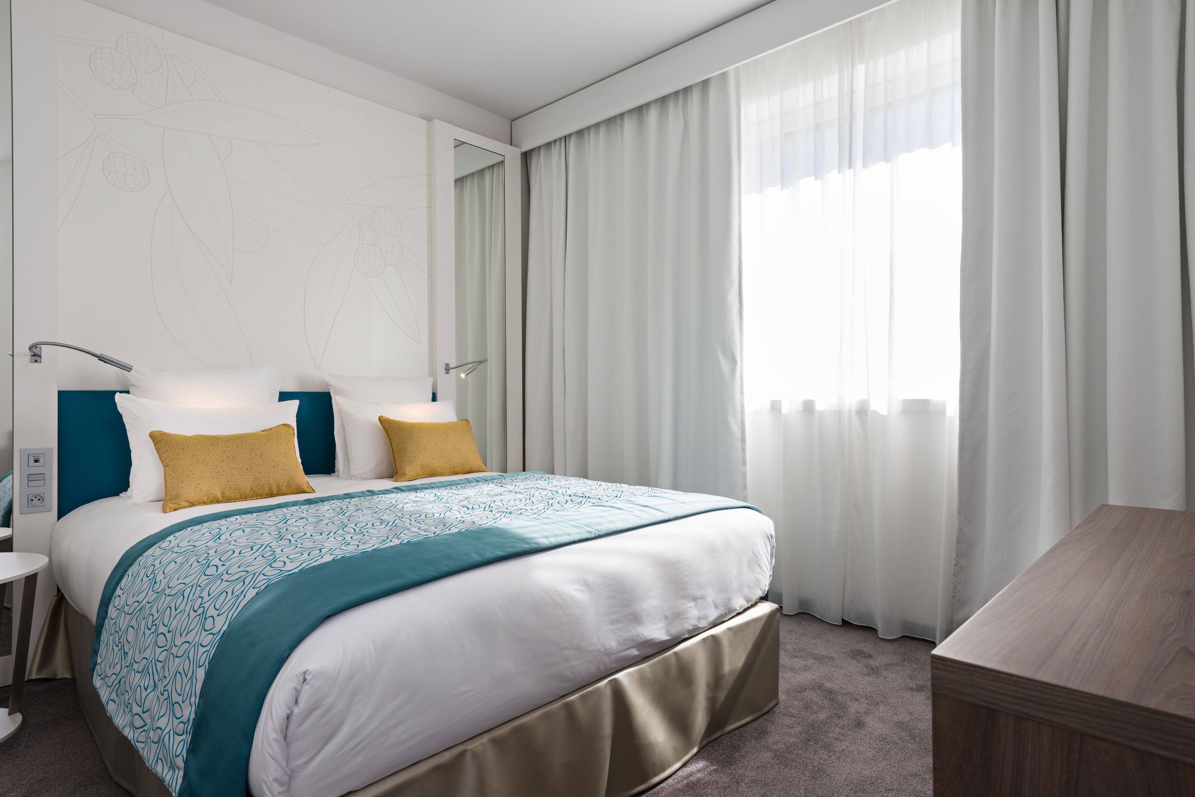Una habitación de hotel moderna con una cama grande, dos mesitas de noche, una mesita auxiliar de madera y un escritorio.