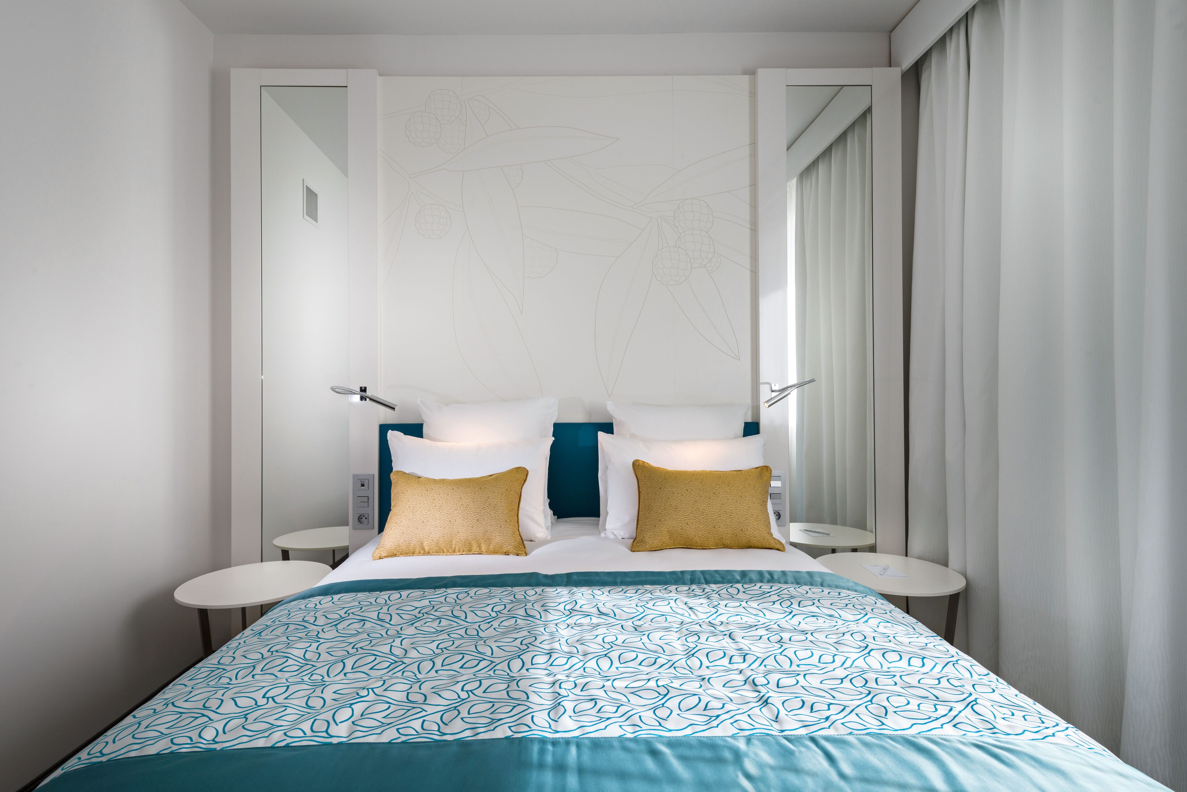 Una habitación de hotel con cama, dos mesitas de noche y un amplio ventanal con cortinas.