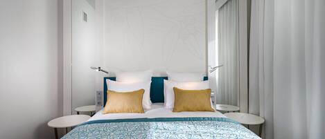 A hotel room with a bed, two bedside tables, and a large window with curtains.