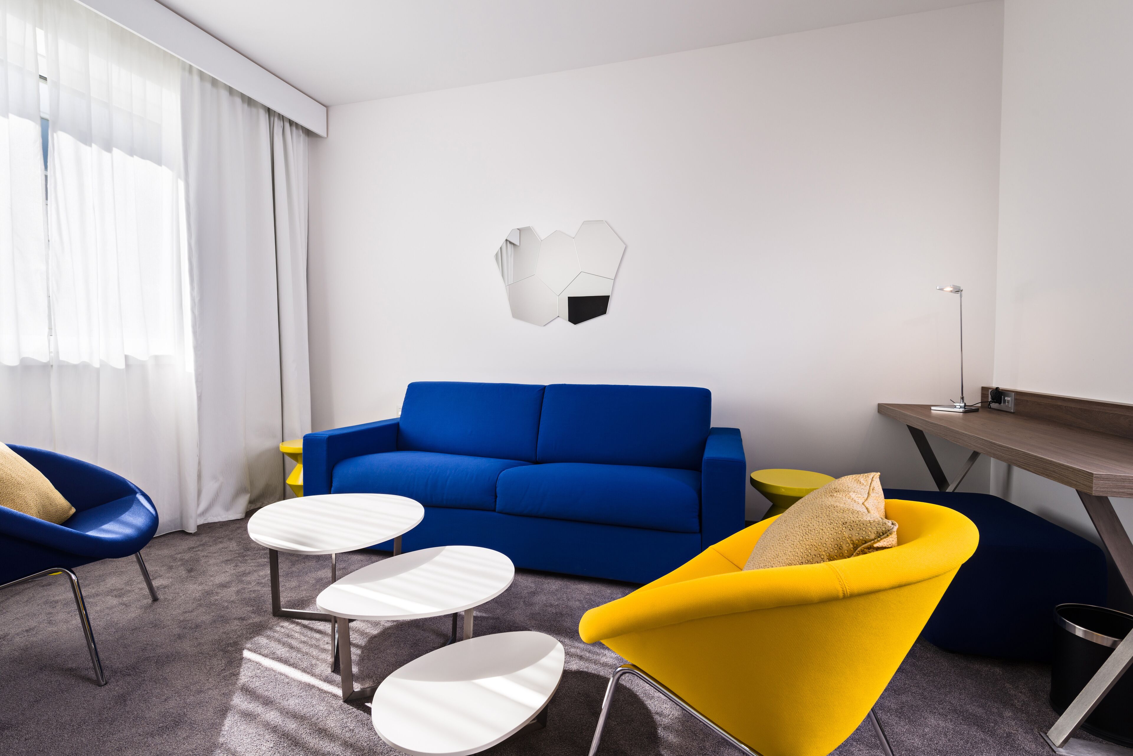 A modern living room with a blue sofa, yellow armchair, and white coffee tables.
