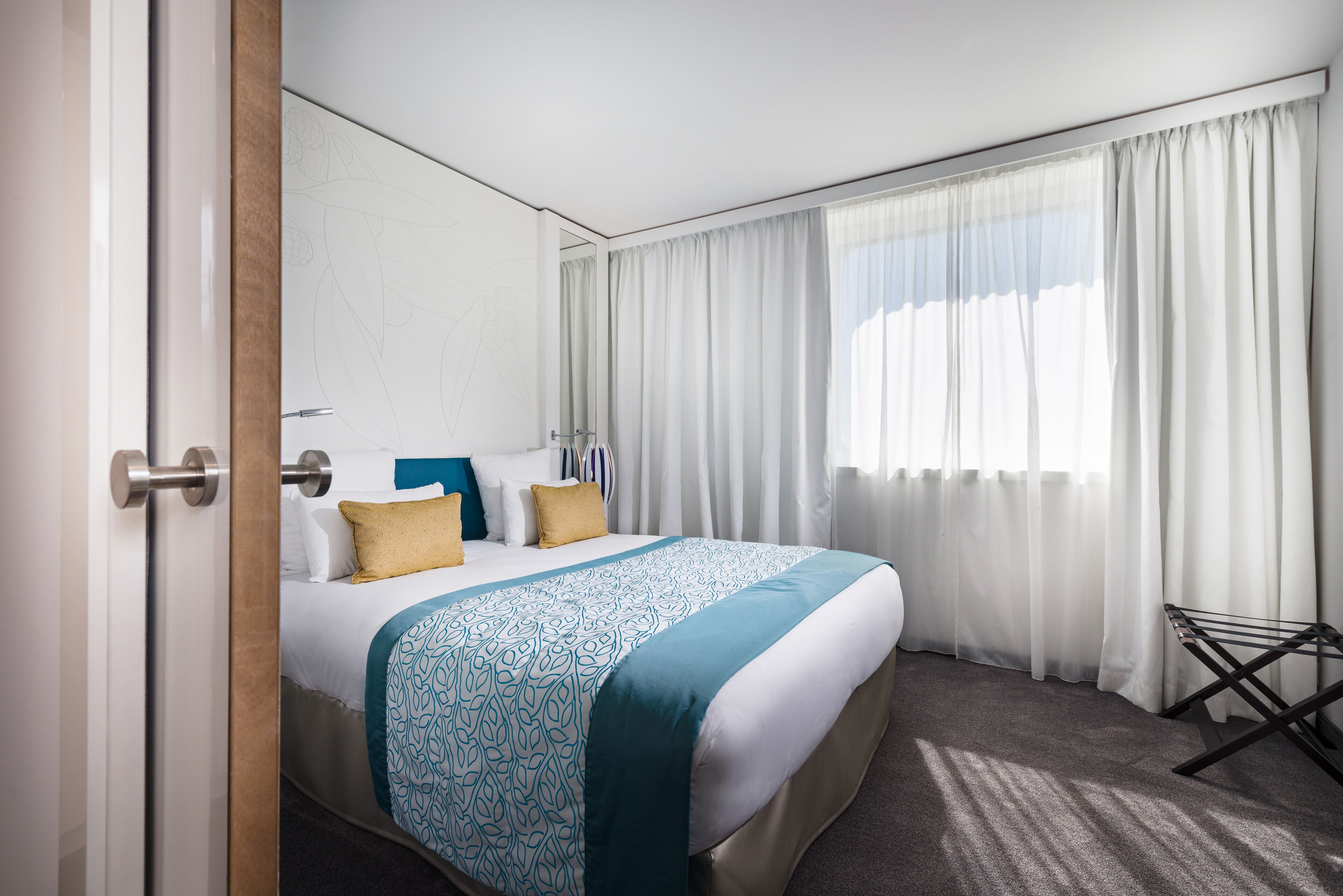 A hotel room with a large bed, white curtains, and a view of the sky.
