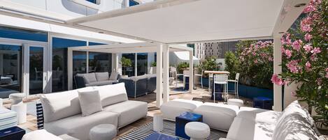 A modern outdoor lounge area with white sofas, blue accents, and a view of the building's exterior.