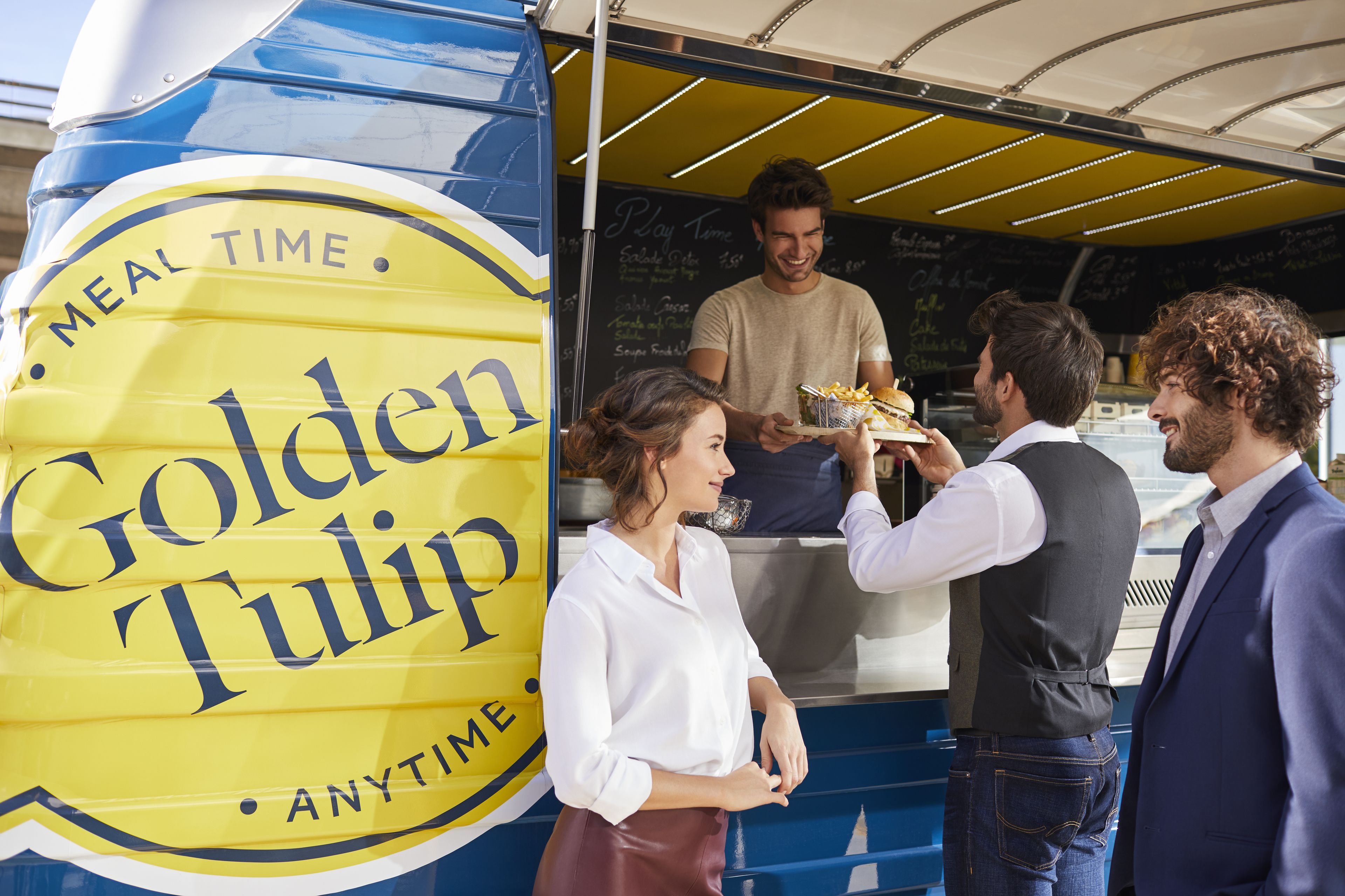 Ein Imbisswagen mit einem gelben Schild, auf dem 'Golden Tulip' und 'ESSENSZEIT. JEDERZEIT.' steht.