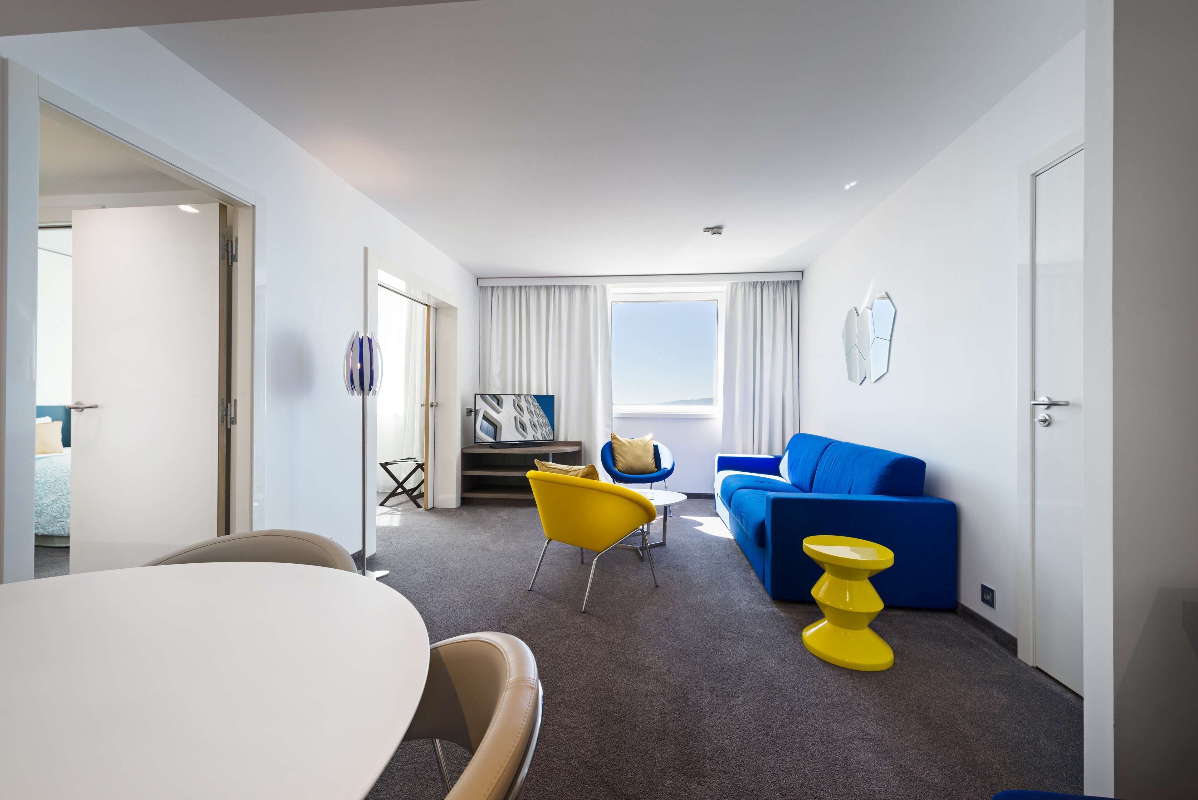 A modern hotel room with a dining area, a sofa, and a yellow side table.