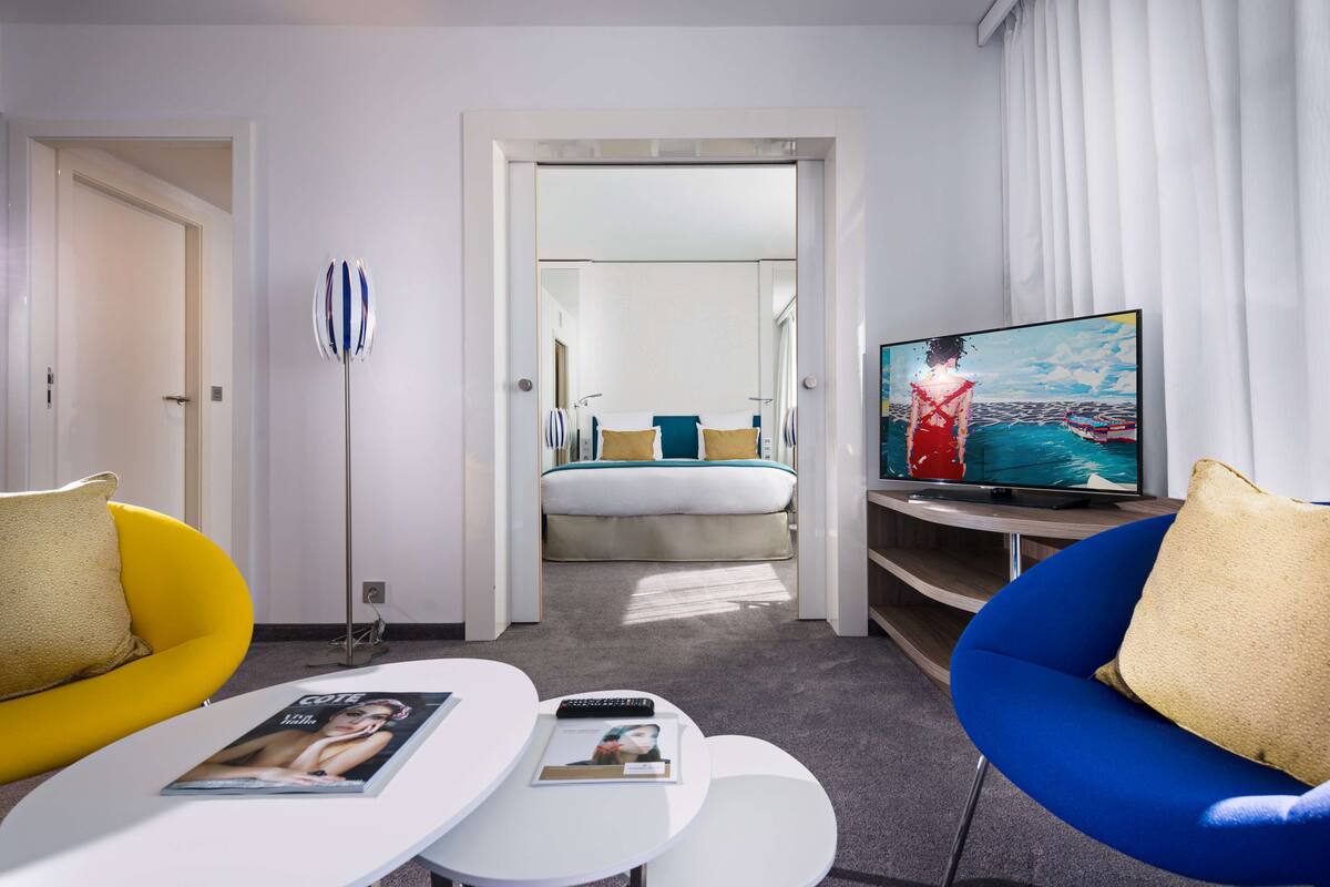 A modern hotel room with a bed, a TV, a sofa, and a small table.
