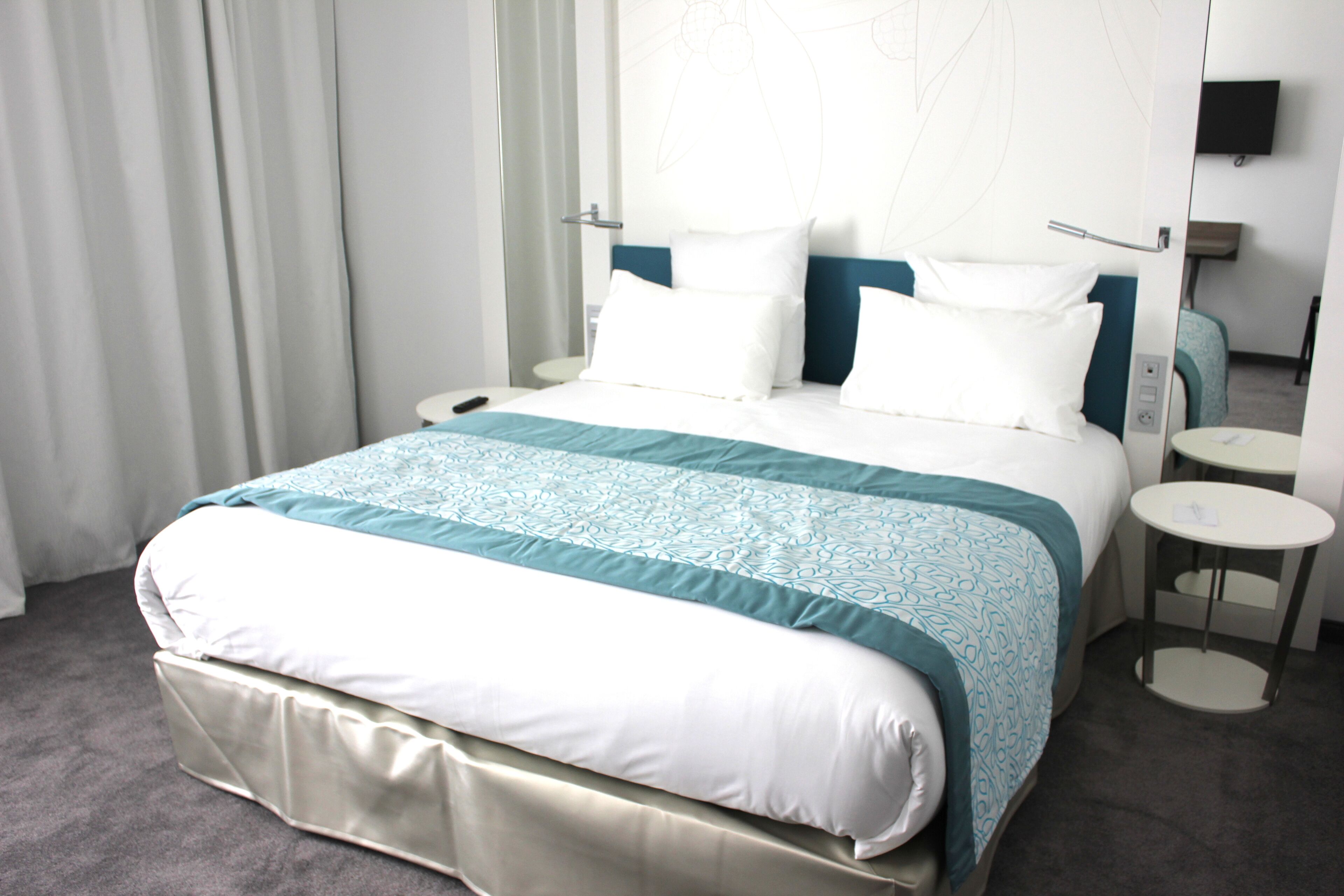 A hotel room with a bed, a bedside table, a chair, a TV, and a window with curtains.