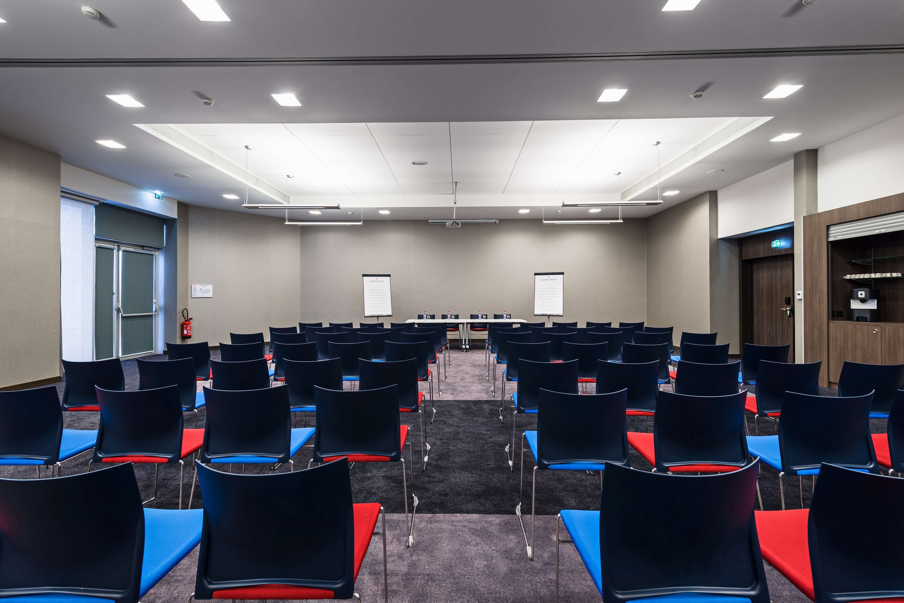 Une salle de conférence avec des rangées de chaises, un écran de projection et un tableau blanc.