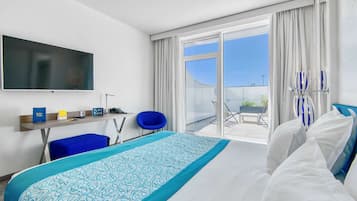 Une chambre d’hôtel avec un grand lit, un téléviseur fixé au mur, un bureau avec une chaise et un balcon avec vue.